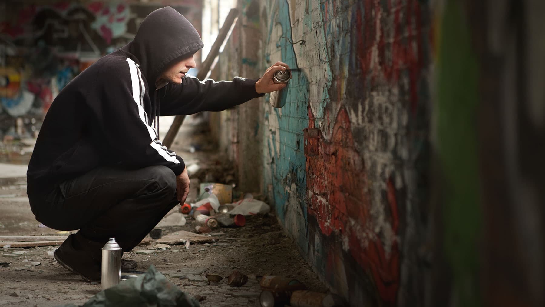 Jongen spuit gehurkt graffiti op een bakstenen muur.